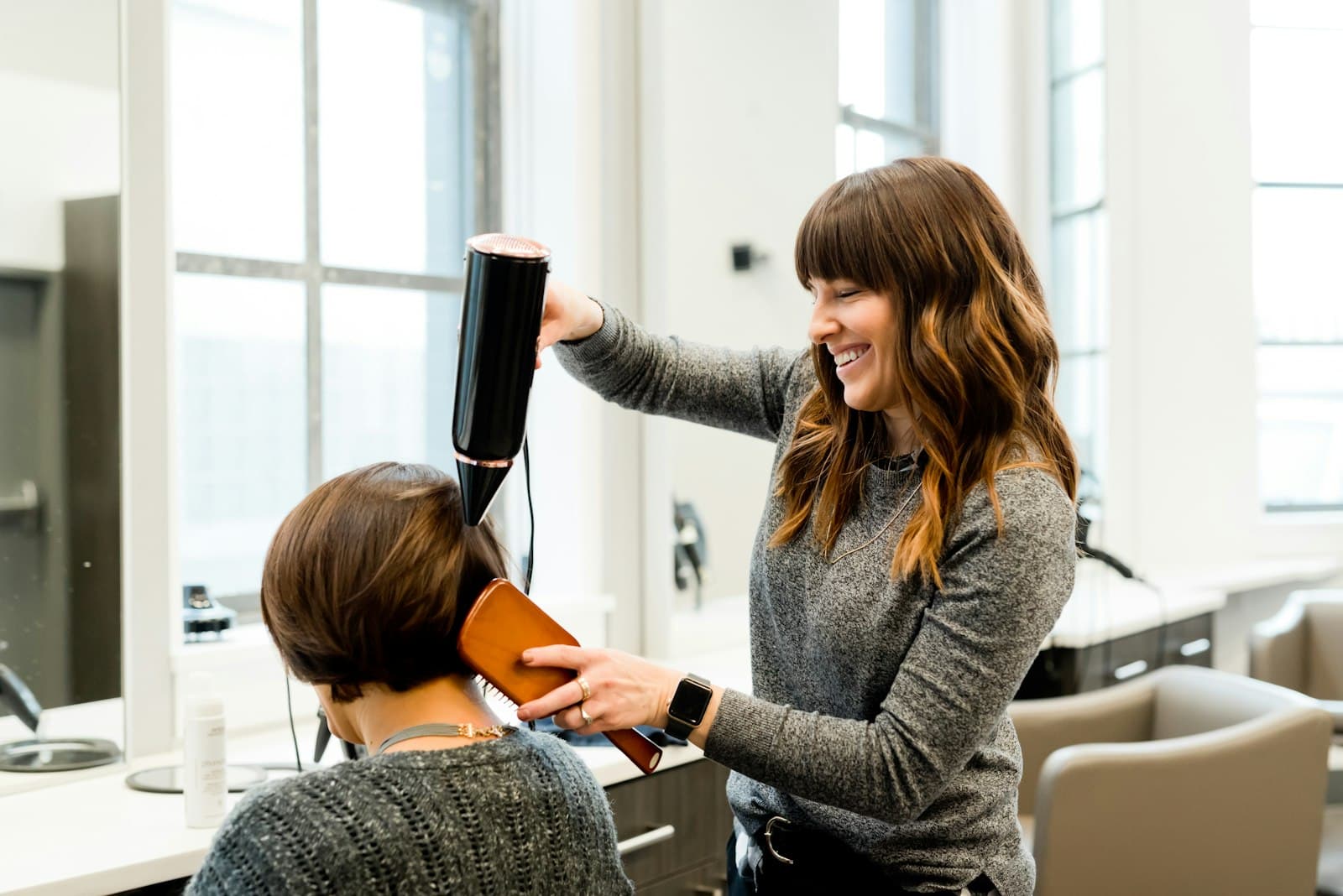 Kapster föhnt het haar van een klant in een lichte, moderne salon