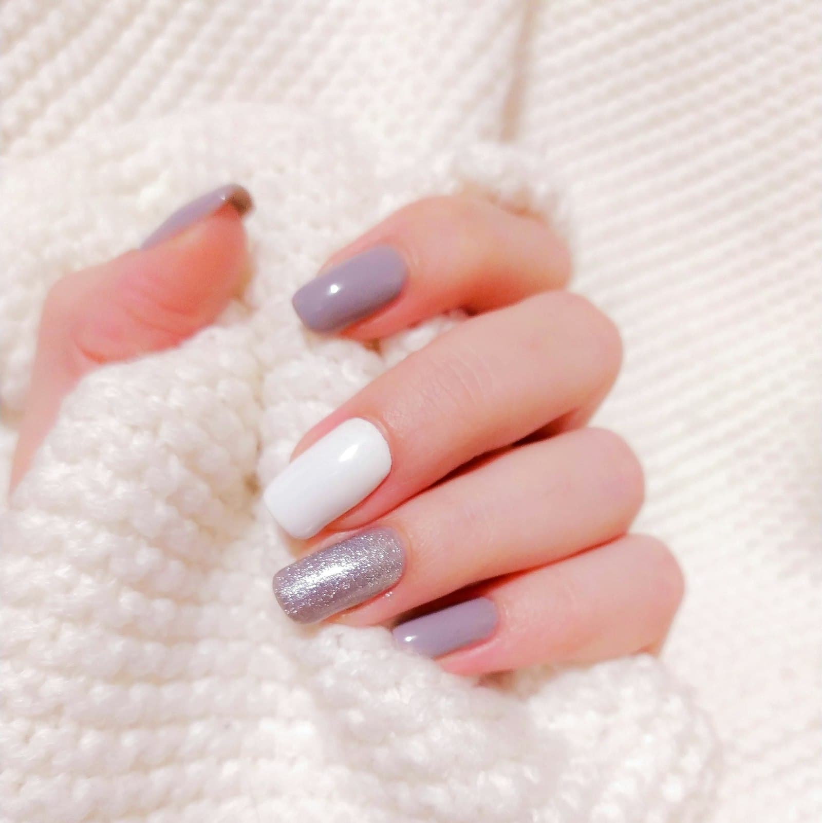 Hand met pastelroze en witte gelnagels op een gebreide trui
