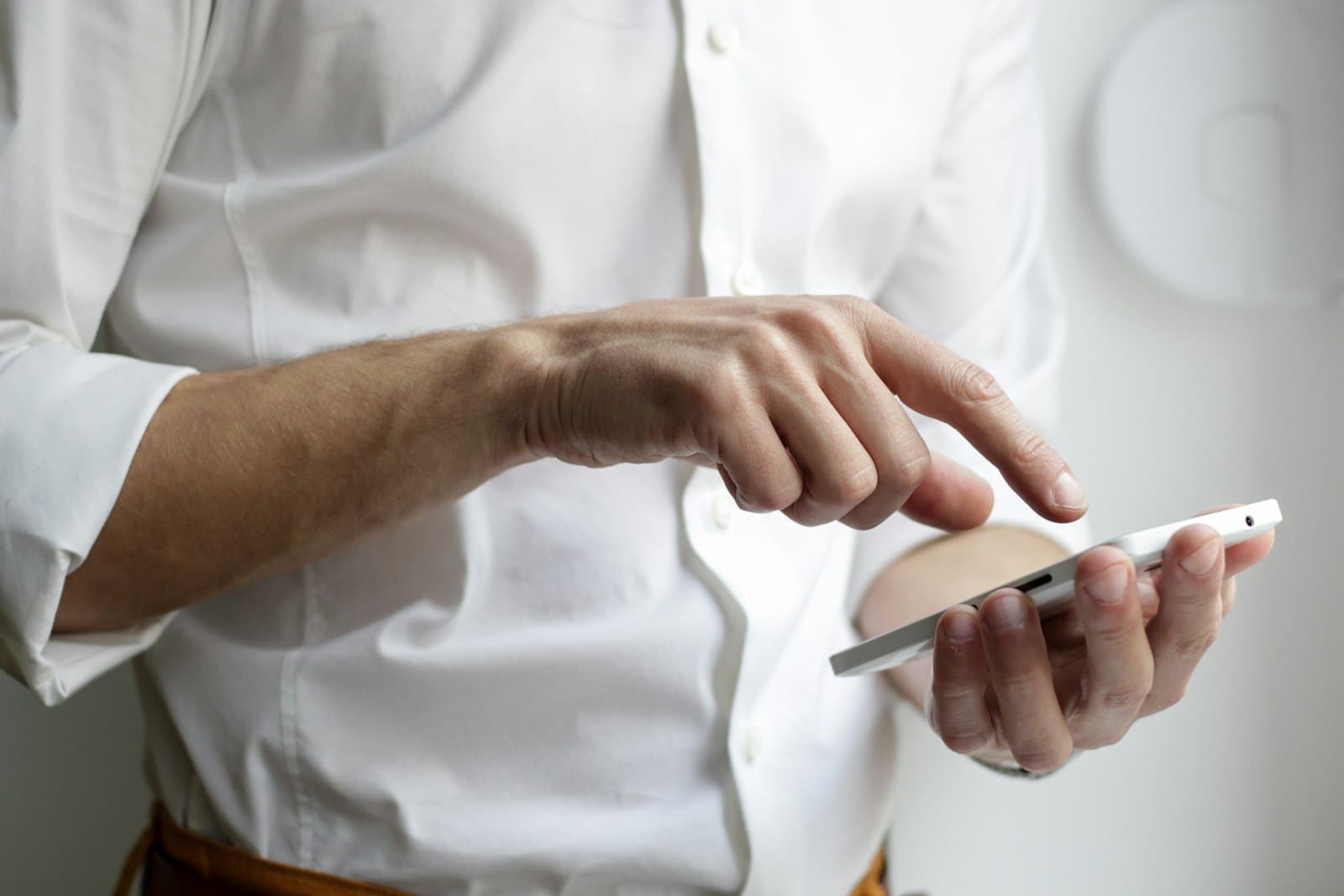 Hand die een smartphone vasthoudt en scrolt, tegen een wit overhemd